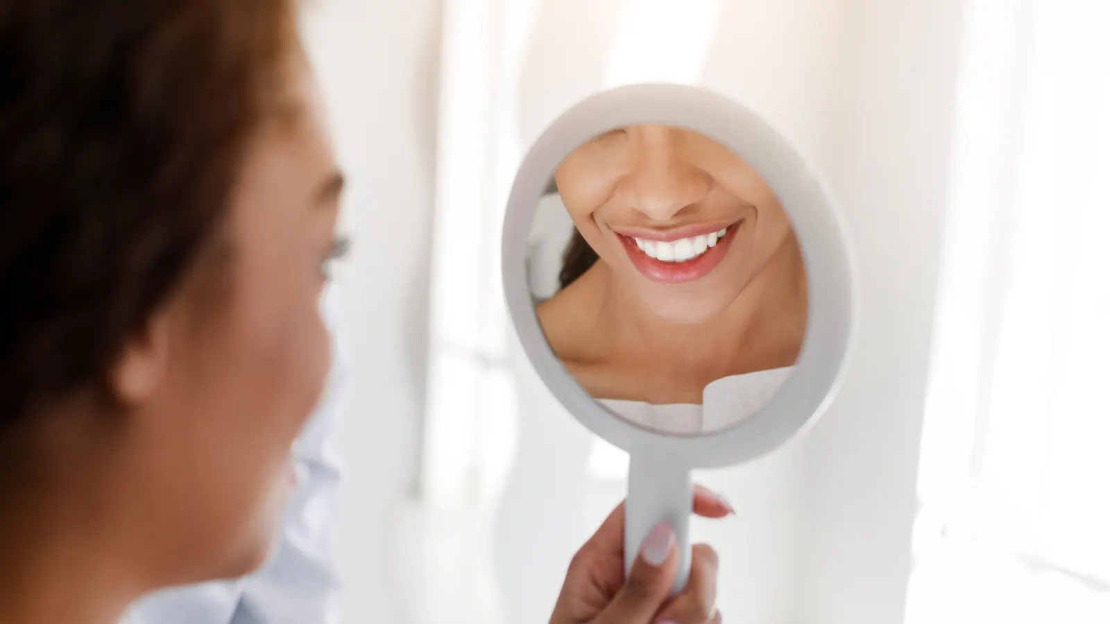 Smiling woman looking at teeth in a mirror