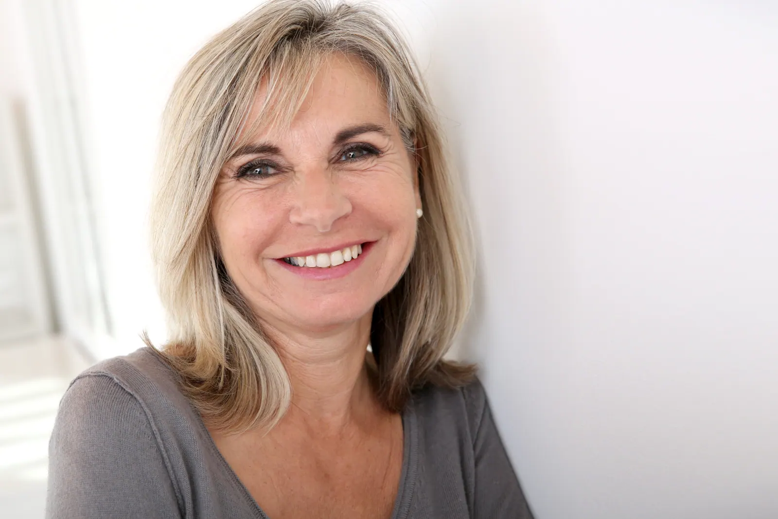 Smiling woman with blonde hair leaning on wall