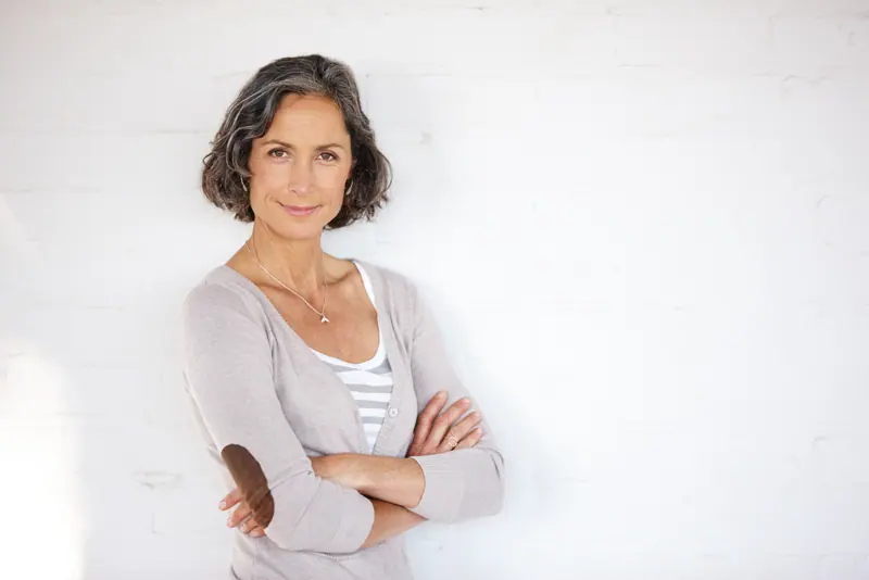 Smiling woman with crossed arms against white wall