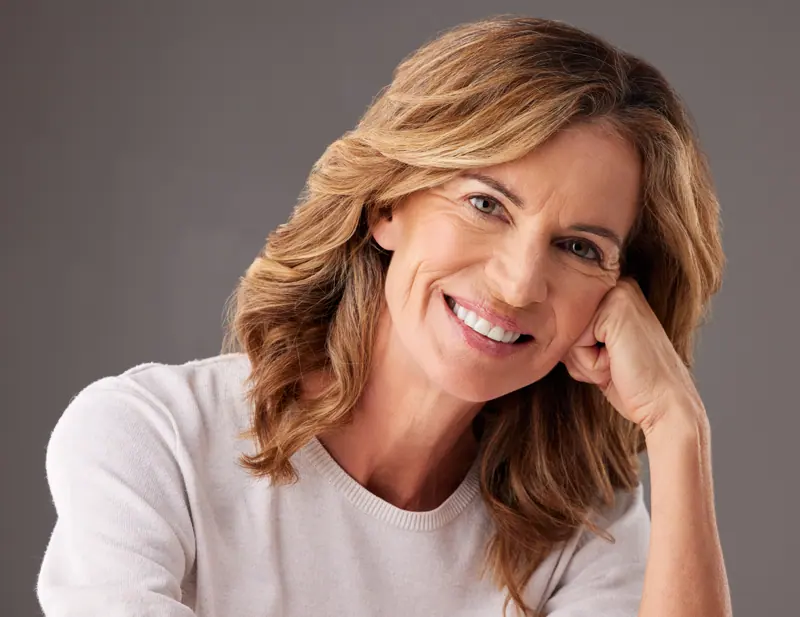 Smiling woman with wavy hair on grey backdrop