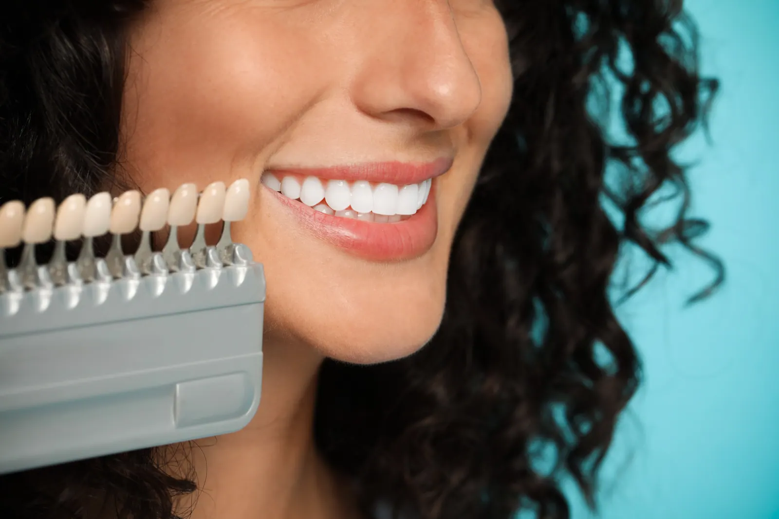 Woman smiling with dental shade guide for teeth wh